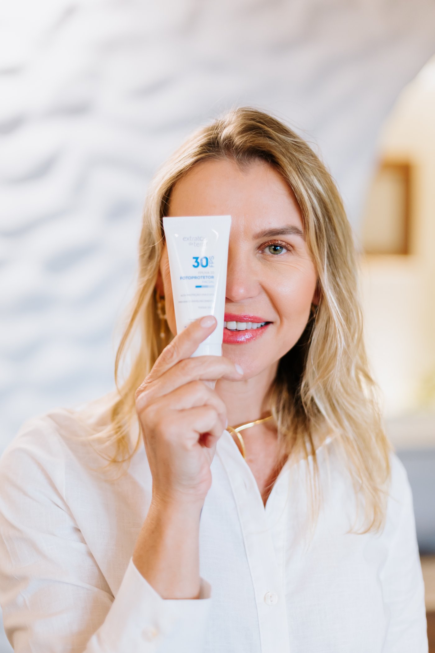 Mulher sorrindo segurando protetor solar facial, pele natural e luminosa