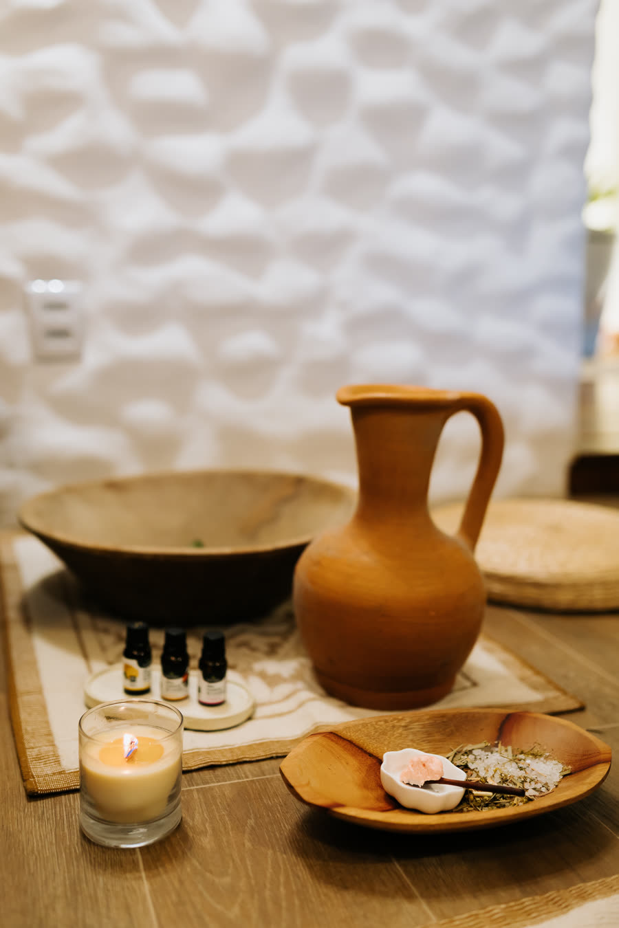 Mesa de preparo do Flow com gamela de madeira, jarro de barro, frascos de óleo, ervas e vela