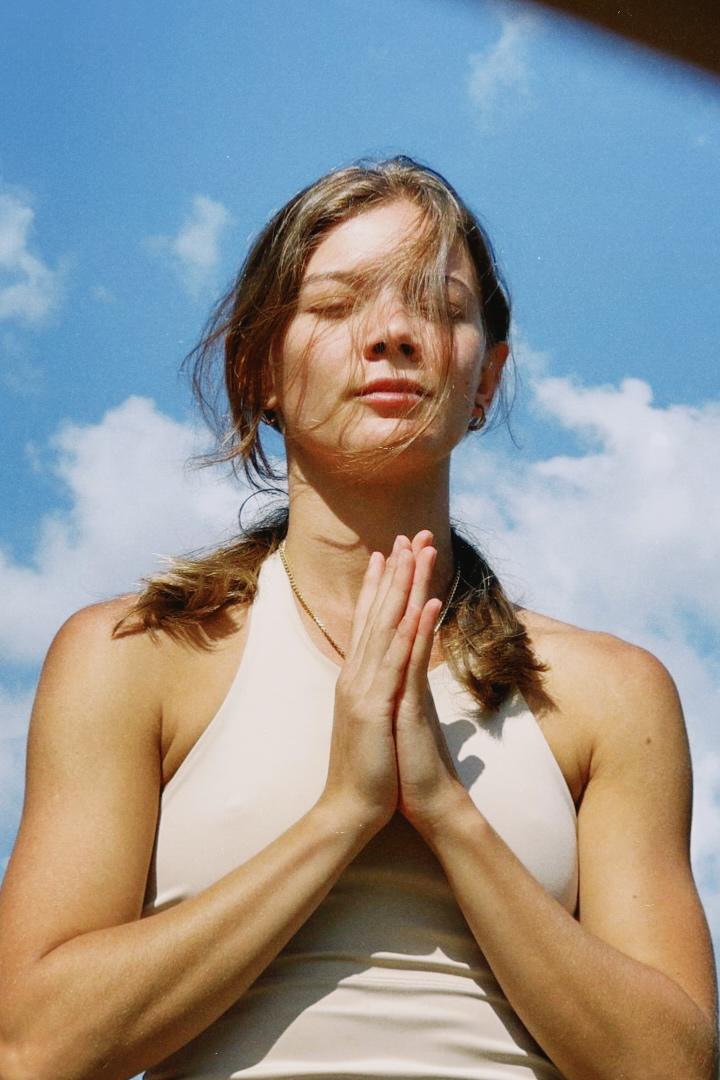 Mulher em meditação ao ar livre, mãos em prece sob o céu